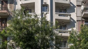 A multi-story building with balconies, a bus stop, and trees in front.