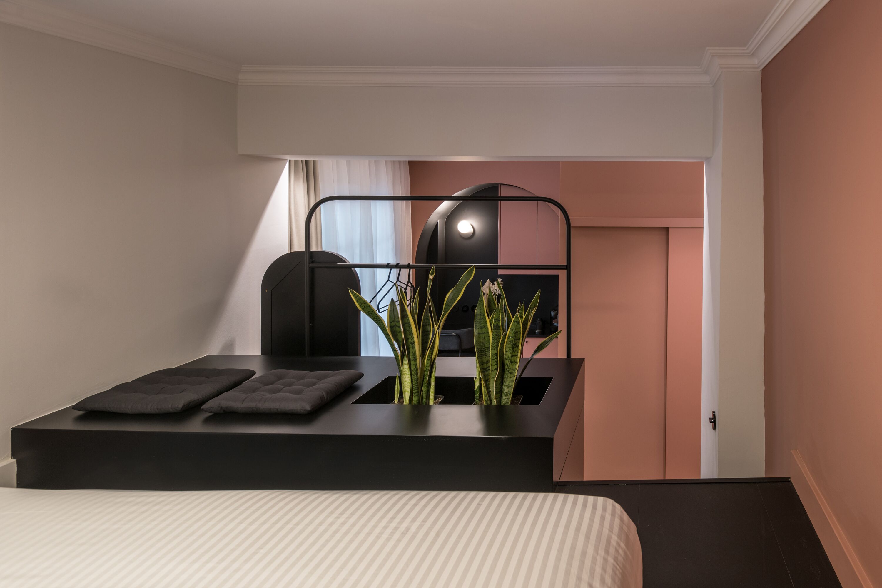 Une chambre d’hôtel moderne comprenant un lit, un bureau avec une chaise, une plante en pot et une armoire.