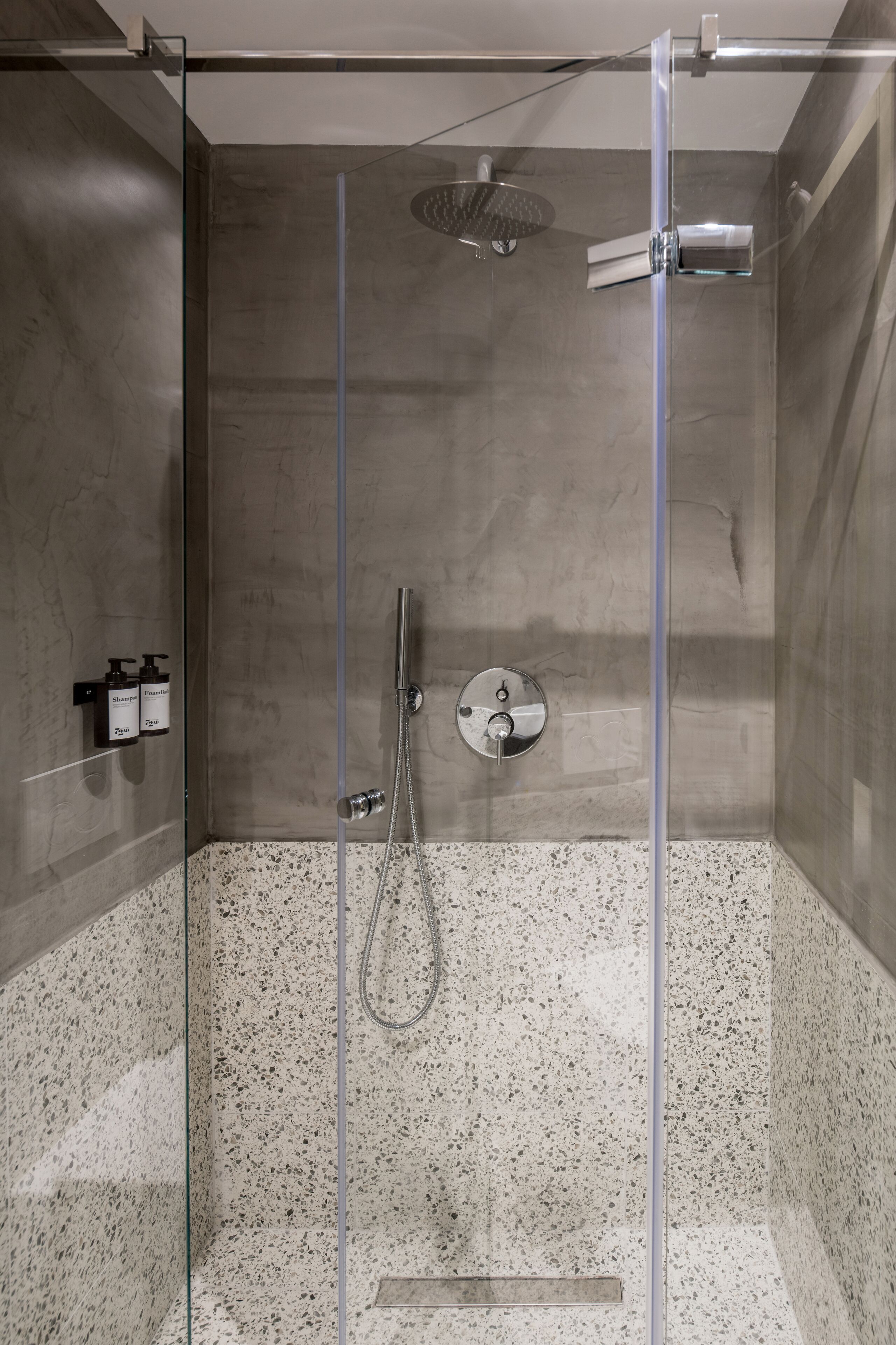 Um chuveiro moderno com porta de vidro, chuveiro manual e painel de controle fixado na parede.