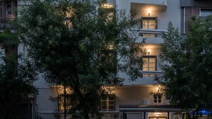 Un edificio de varios pisos con balcones, una entrada a nivel de calle y un refugio de autobús.