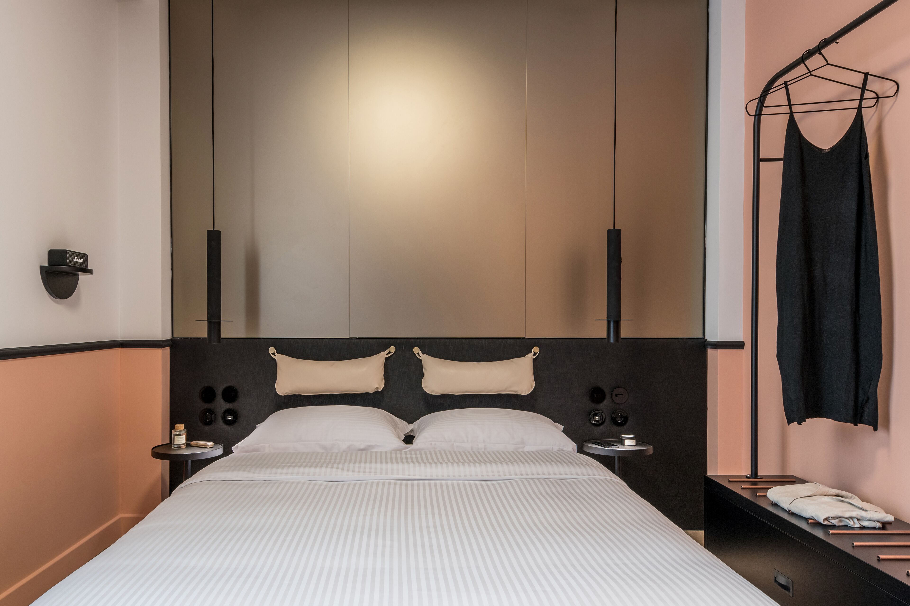 A modern hotel room with a large bed, two bedside tables, a hanging towel rack, and a minimalist design.