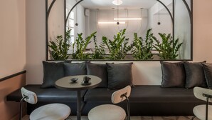 Una habitación moderna con un sofá negro, dos sillones, una mesita redonda y un espejo grande sobre el sofá.