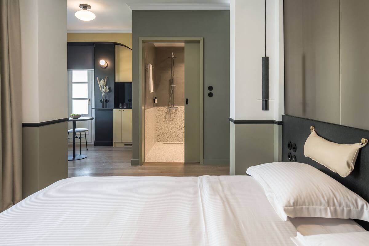 Una habitación de hotel moderna con una cama grande, un baño independiente con ducha y una pequeña zona de kitchenette.