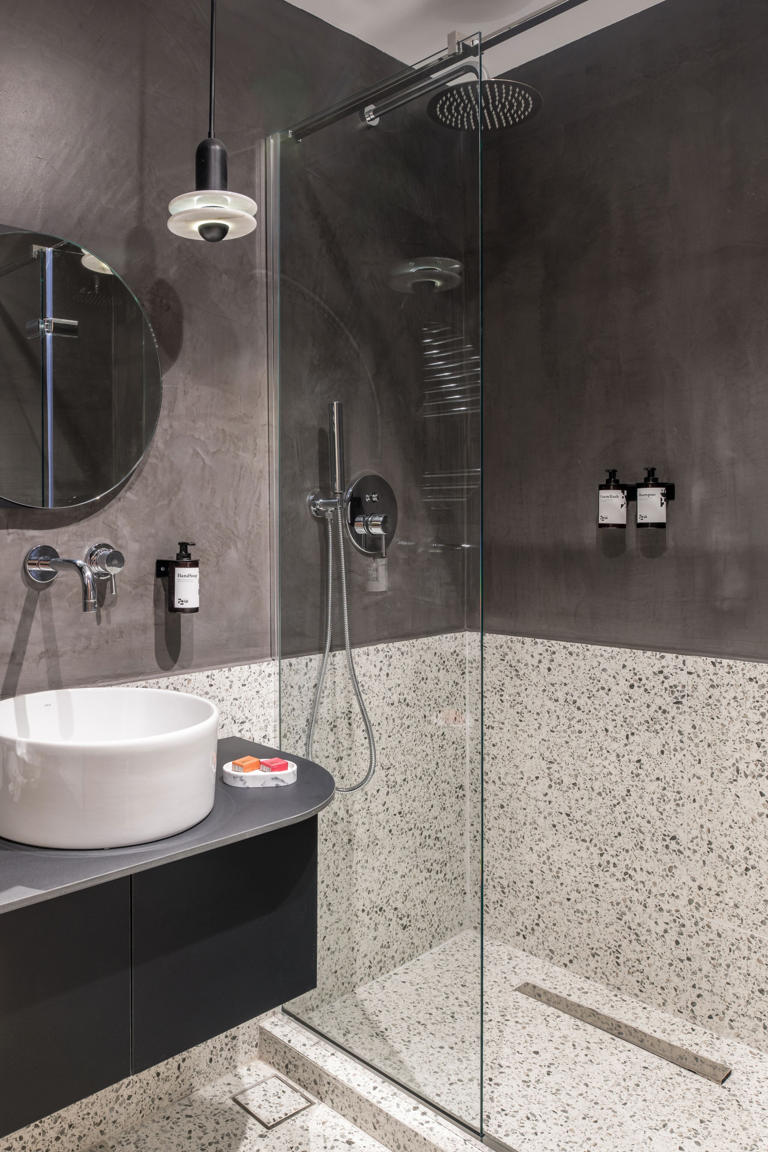 Une salle de bain moderne avec une douche à parois de verre, un miroir rond et un lavabo blanc.