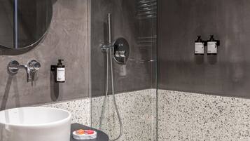 Une salle de bain moderne avec une douche à parois de verre, un miroir rond et un lavabo blanc.