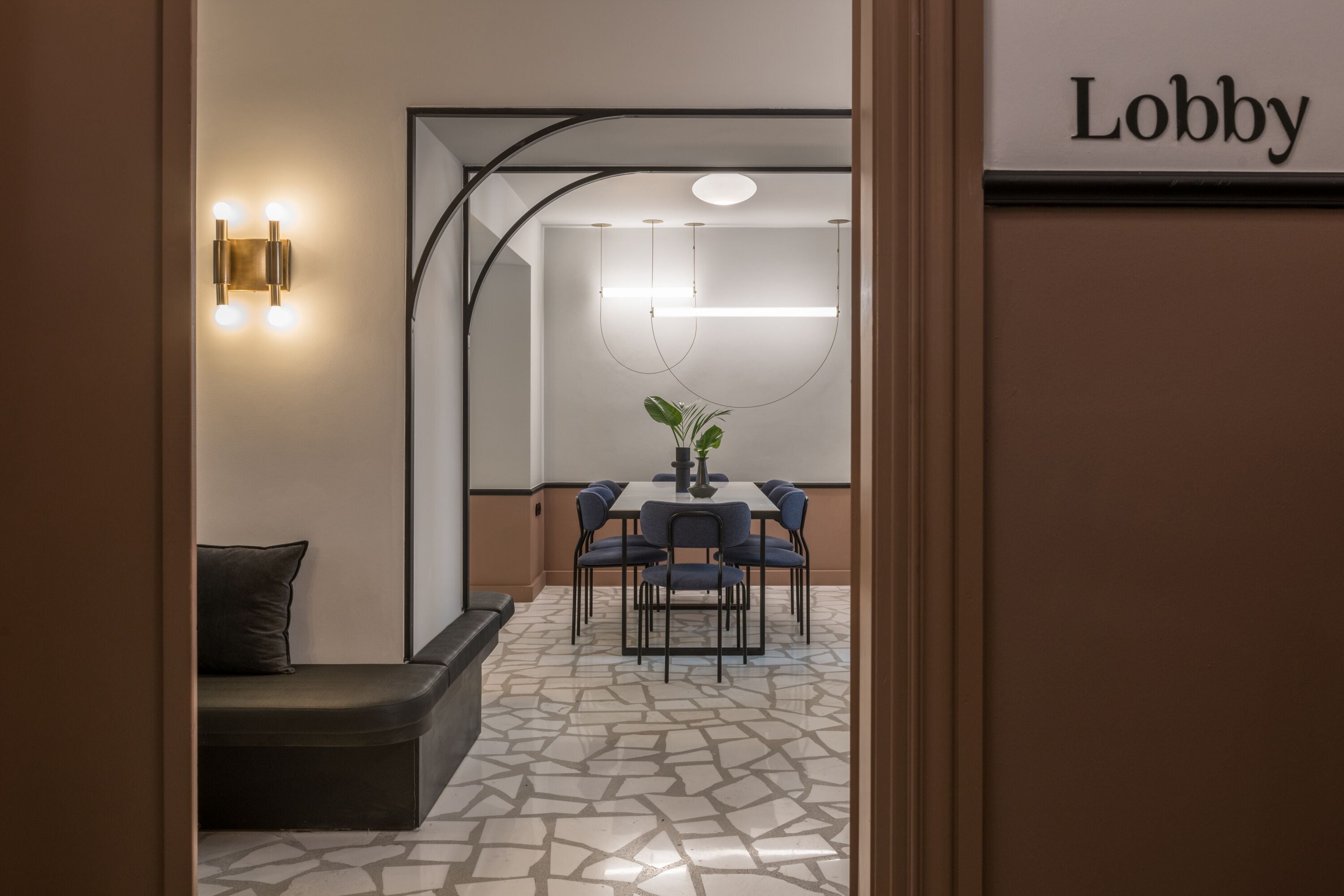 Um lobby com design moderno, com área de estar com sofá e cadeiras, uma mesa de jantar com cadeiras, e uma placa indicando a área do lobby.