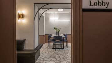 Um lobby com design moderno, com área de estar com sofá e cadeiras, uma mesa de jantar com cadeiras, e uma placa indicando a área do lobby.