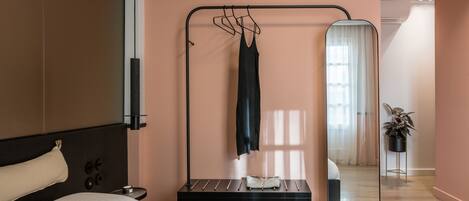 A modern bedroom with a bed, a hanging clothes rack, a bedside table, and a mirror.