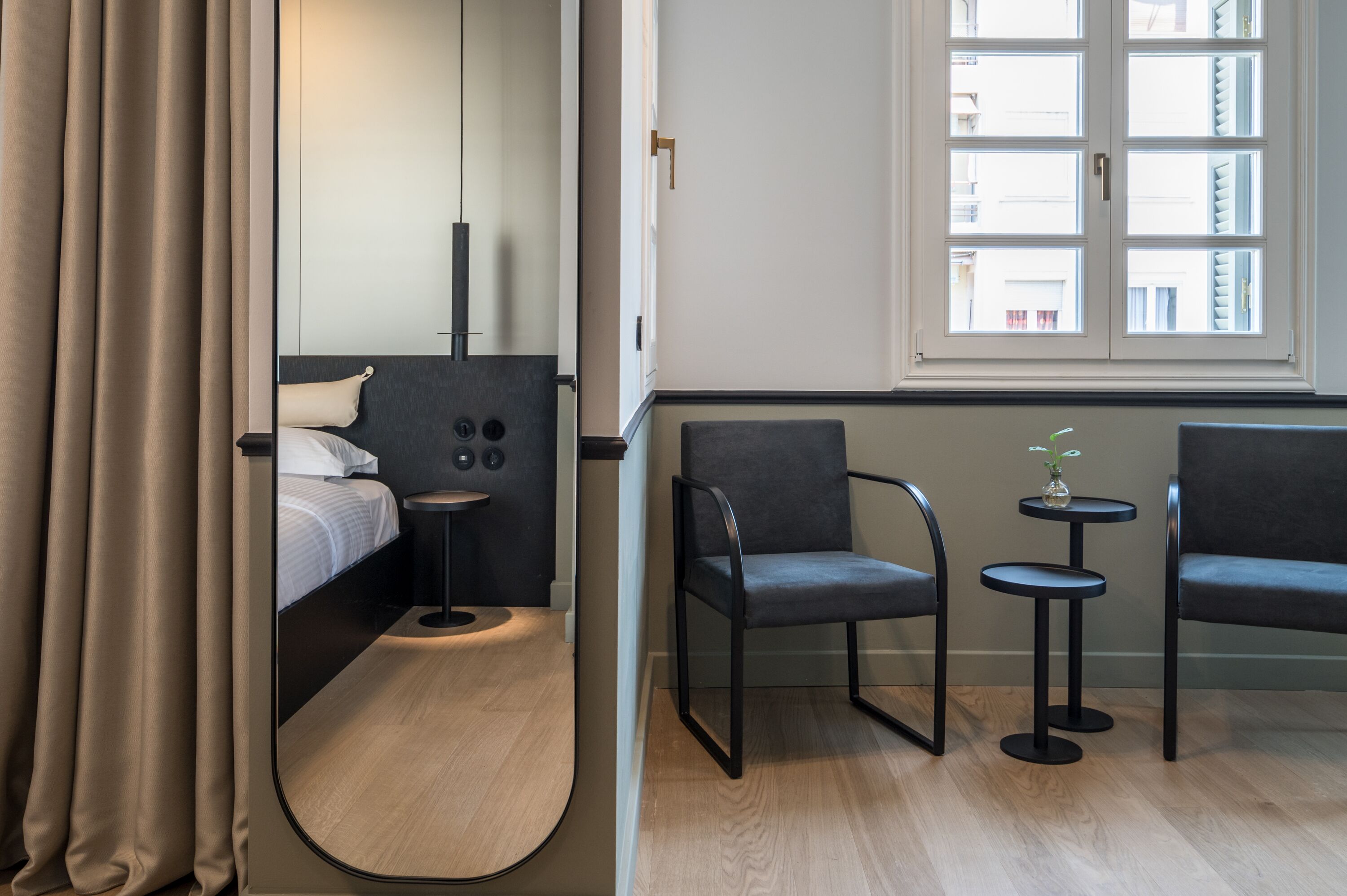 A modern hotel room with a bed, two chairs, a small table, and a large mirror.