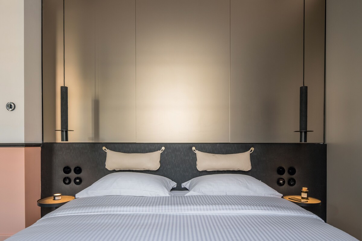 A modern hotel room with a large bed, bedside tables, and a headboard with integrated lighting.