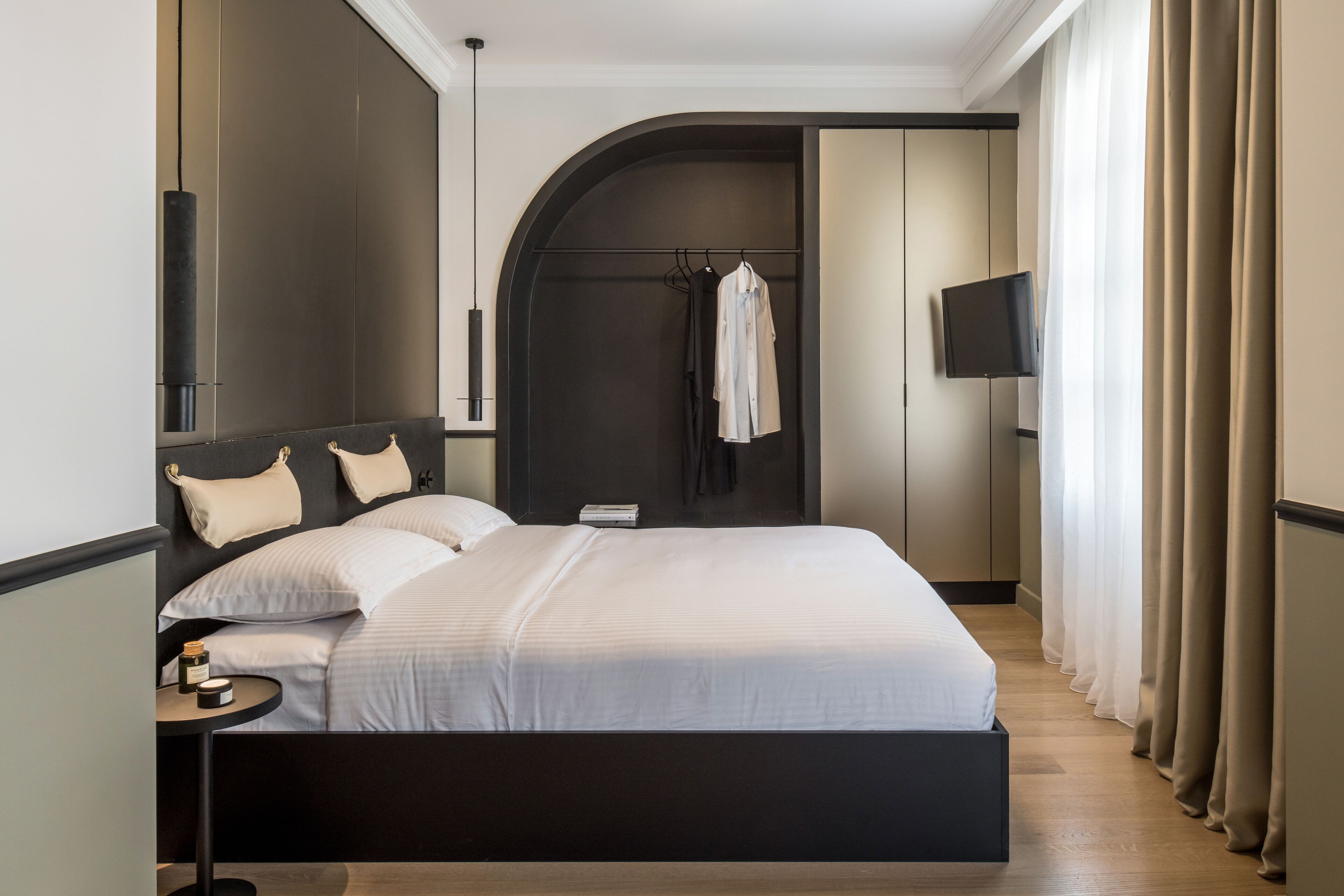 Et moderne hotelværelse med en stor seng, et sengebord, et vægmonteret tv og et knagered.