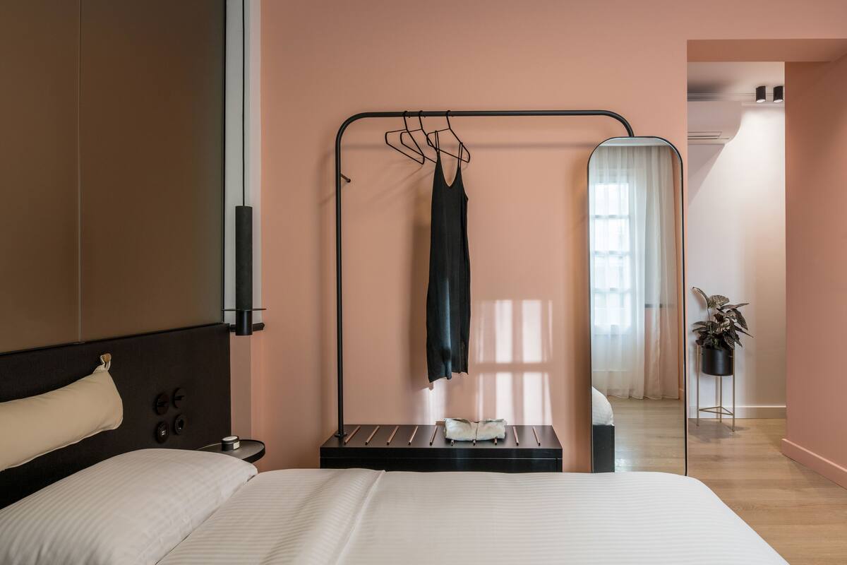 Un dormitorio con cama, perchero, mesita de noche y espejo.