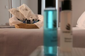 A neatly arranged basket of toiletries on a bed with a clear bottle of water in the foreground. - Lavender Otel (Cesme)