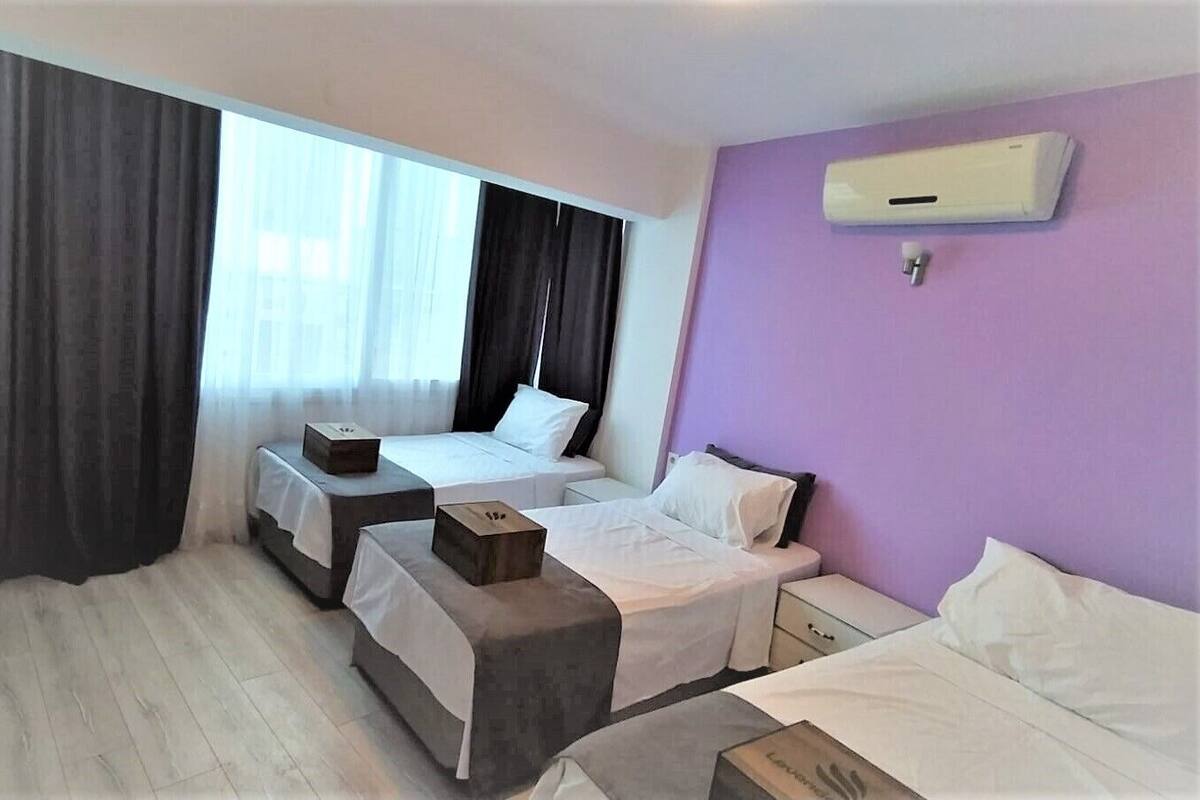 A hotel room with two beds, a window with curtains, a wall-mounted air conditioner, and a wooden nightstand.