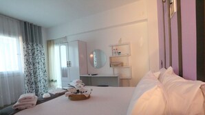 Une chambre d’hôtel comprenant un lit, une table de chevet avec des serviettes, un miroir, une étagère avec des articles de toilette et une fenêtre avec des rideaux.