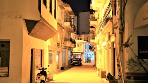 Une rue étroite, bordée de bâtiments des deux côtés, avec un scooter garé et une voiture au loin.