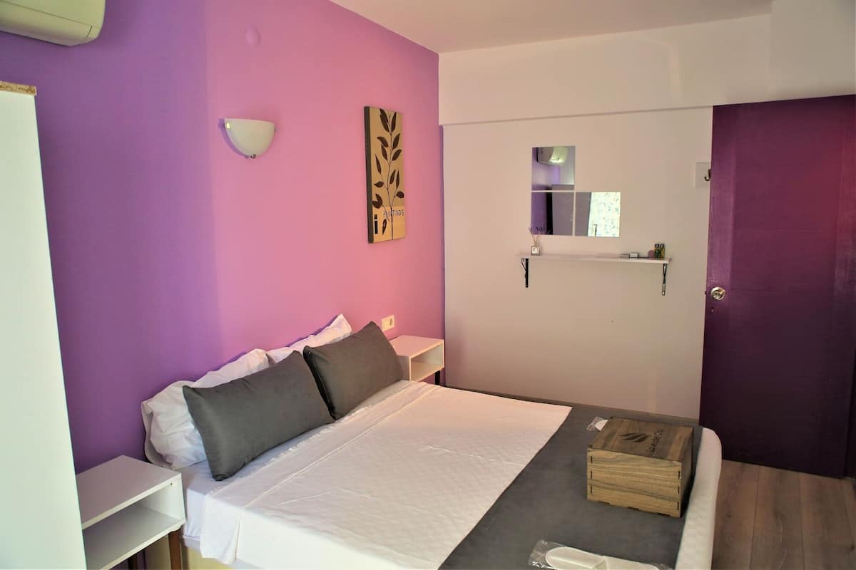 A bedroom with a bed, a nightstand, a wall-mounted light, a mirror, and a door.