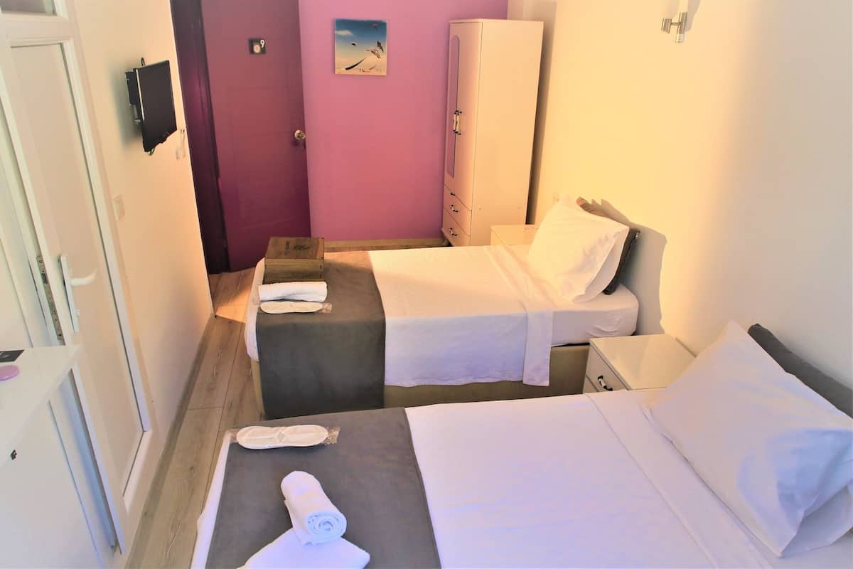 A small hotel room with two beds, a wardrobe, a desk, and a bathroom.