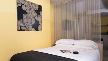 Habitación de hotel con cama, un cuadro abstracto en blanco y negro en la pared y una ventana con cortinas traslúcidas.