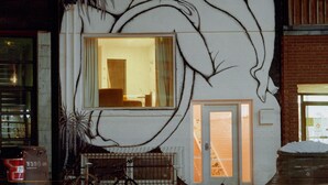 A building with a large mural of a reclining figure, a visible window, and a bicycle parked outside. - Ode (Toronto)