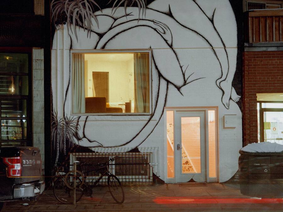A building with a large mural of a reclining figure, a visible window, and a bicycle parked outside.