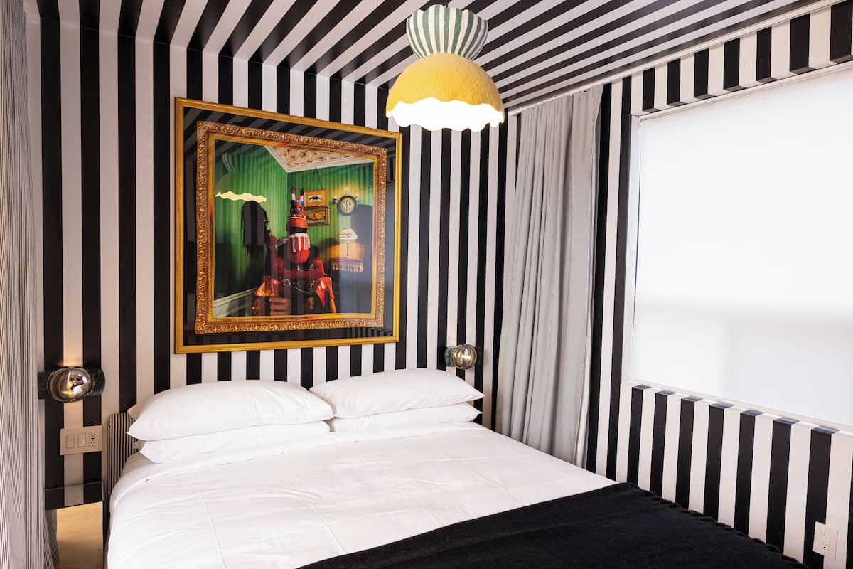 Um quarto com uma cama, um quadro emoldurado, uma luminária e uma janela.