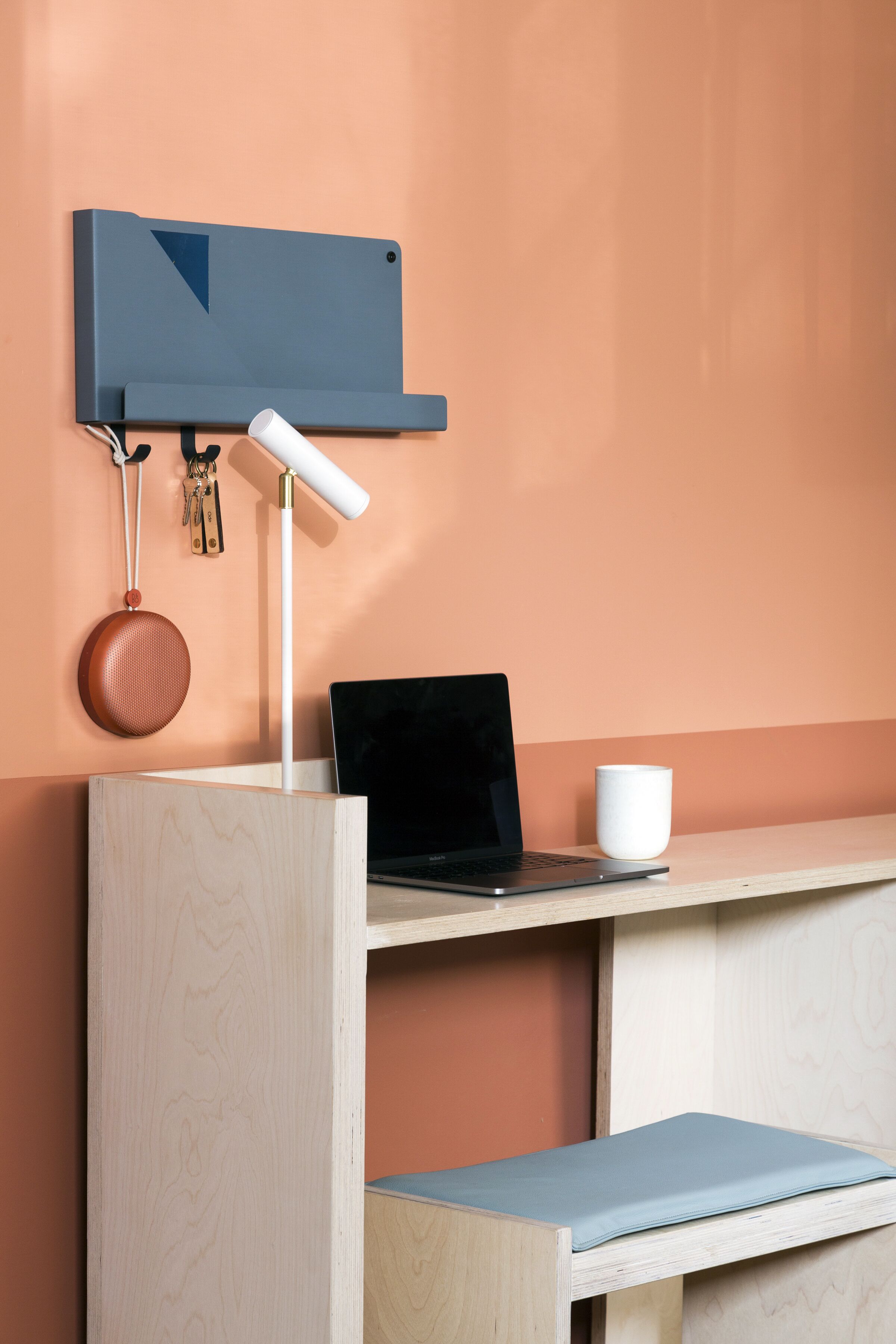 A wooden desk with a laptop, a white mug, and a hanging organizer with keys and a round object.