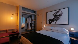 A hotel room with a bed, a seating area, a wardrobe, and a large framed artwork on the wall. - Ode (Toronto)
