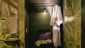 A compact bathroom with a wooden bench, a hanging robe, and a suitcase on the bench. - Ode (Toronto)