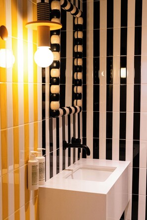 A modern bathroom with a white sink, black and white striped wall tiles, and a unique light fixture with round bulbs.