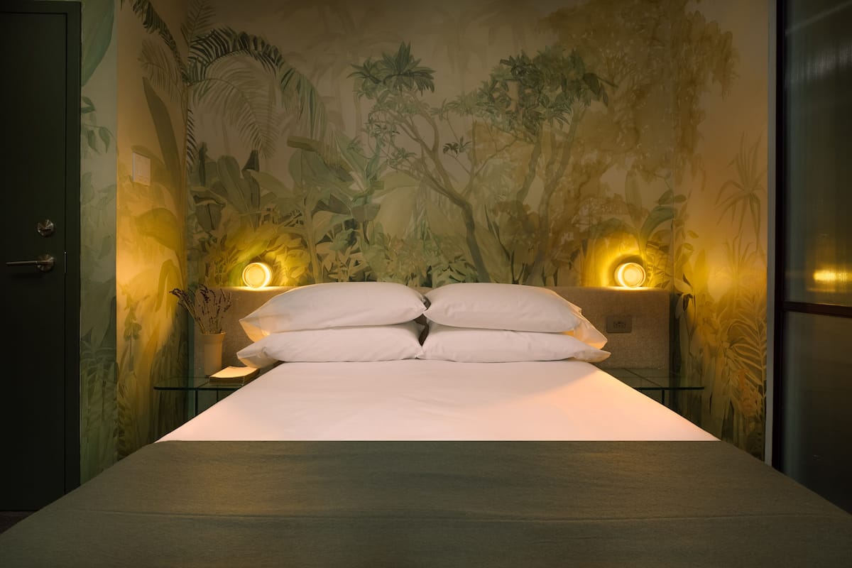 Cama com lençóis brancos e duas luminárias fixadas nas paredes, uma de cada lado.