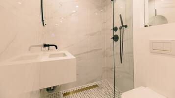 Un baño moderno con ducha de vidrio, un lavabo blanco y pared de mármol.