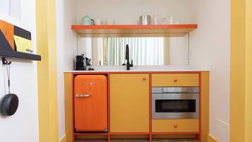 A compact kitchen with a vintage orange refrigerator, a built-in oven, and a stainless steel sink.