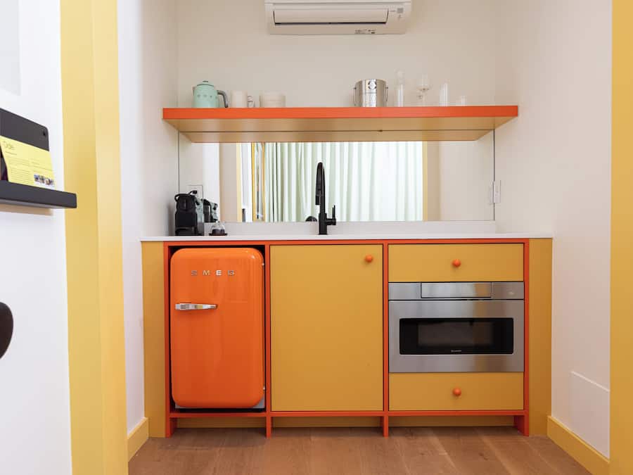 Una cocina compacta con un refrigerador naranja antiguo, un horno empotrado y un lavamanos de acero inoxidable.