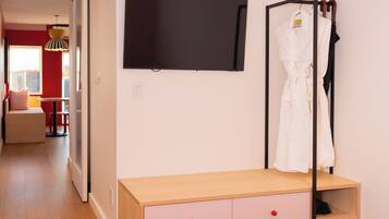 A bedroom with a bed, a TV mounted on the wall, a wooden dresser with drawers, and a robe hanging on a rack.