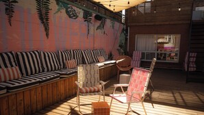 A wooden deck with a striped sofa, two wicker chairs, and a small orange ottoman. - Ode (Toronto)