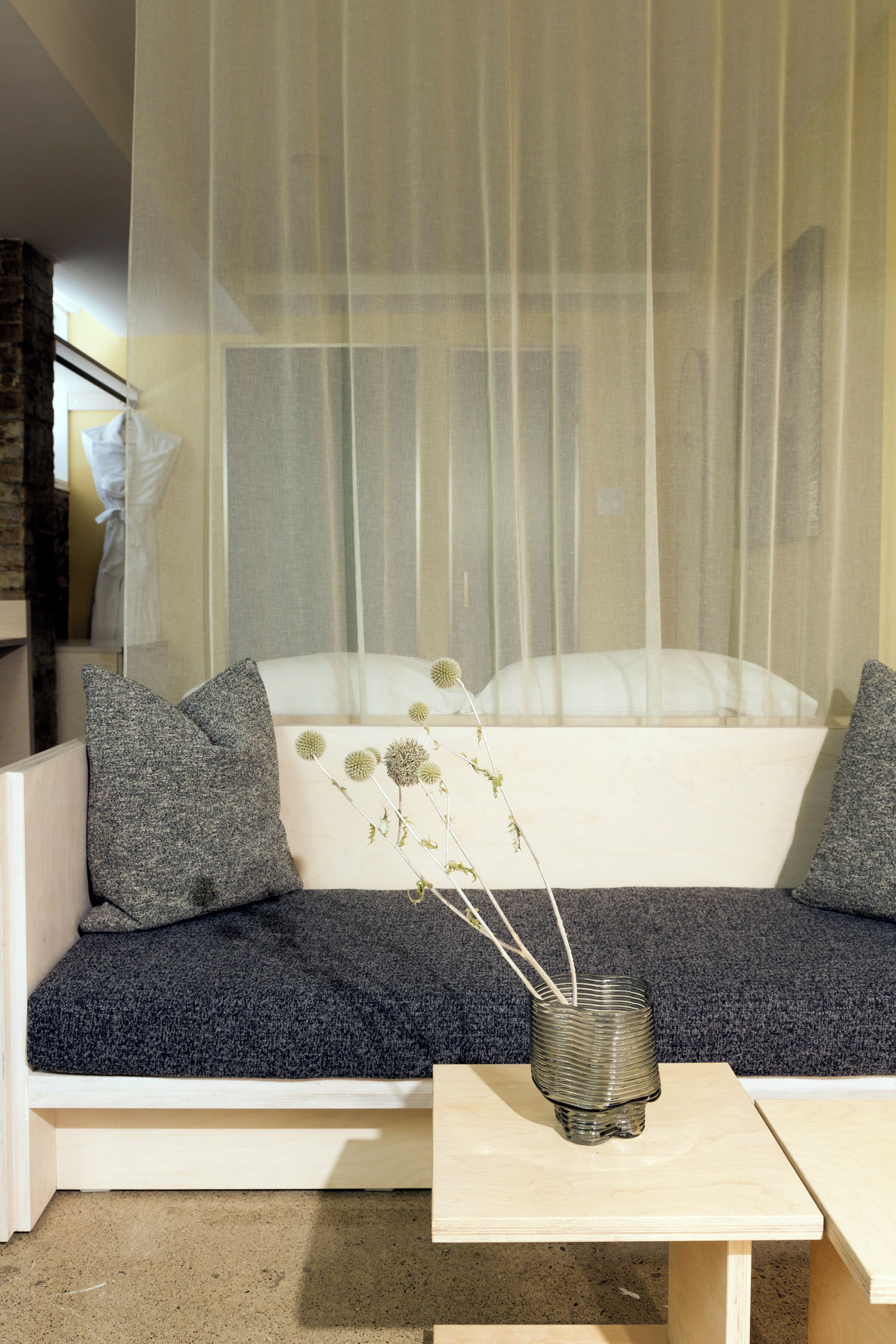 A modern living room with a white sofa, grey cushions, and a small table with a vase of dried flowers.
