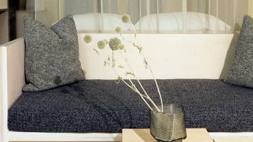 A modern living room with a white sofa, grey cushions, and a small table with a vase of dried flowers.