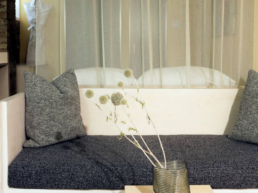 A modern living room with a white sofa, grey cushions, and a small table with a vase of dried flowers.