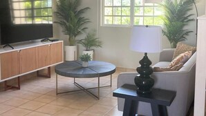 Una sala de estar con televisor, sofá, una mesita y dos plantas en macetas.