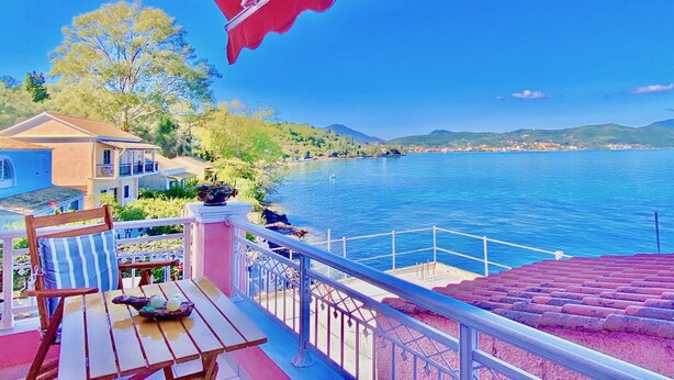 Un balcó amb vista a un llac, una taula de dinar i un parasol vermell.