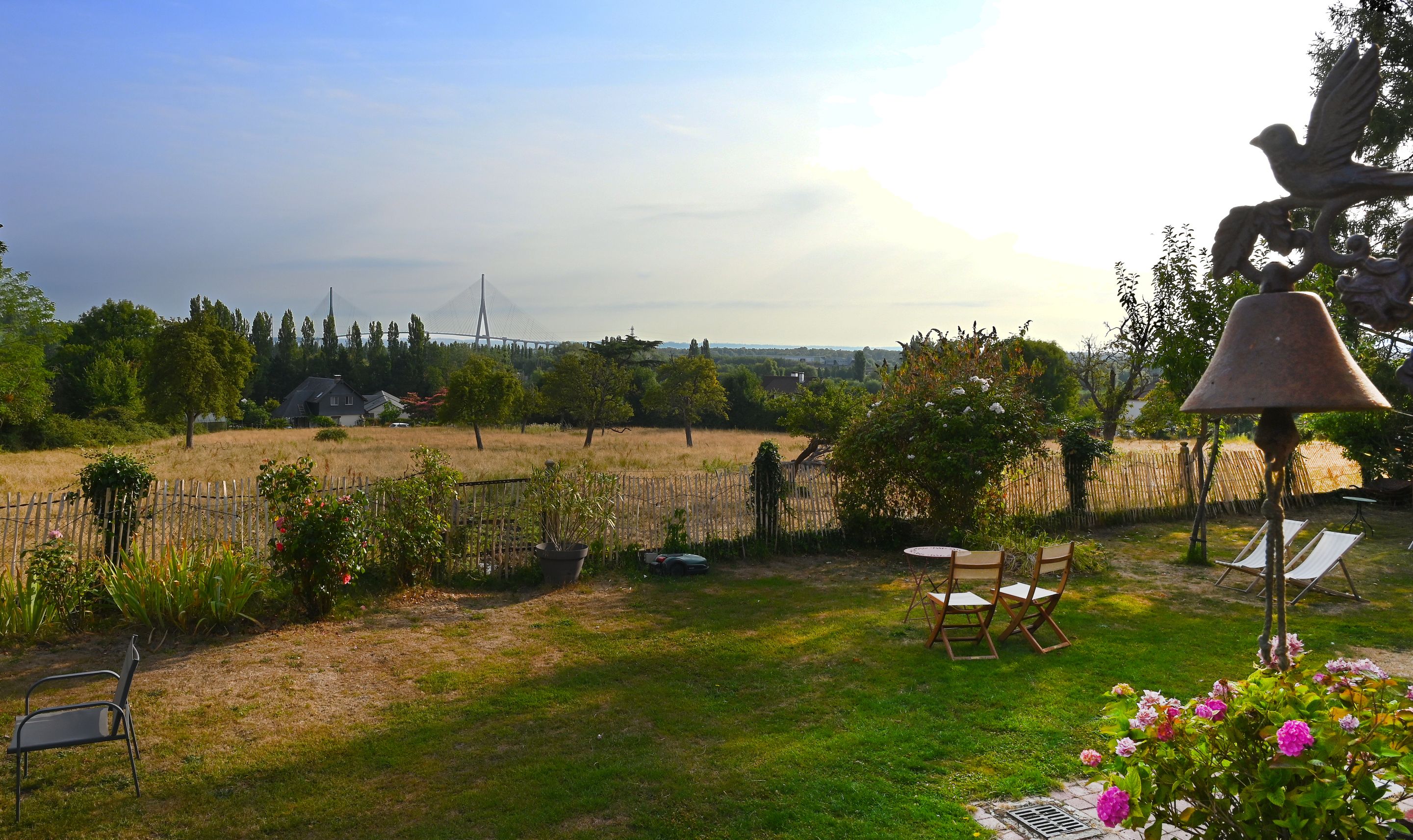 Ein Garten mit Blick auf eine Brücke, eine Glocke und Sitzgelegenheiten im Freien.
