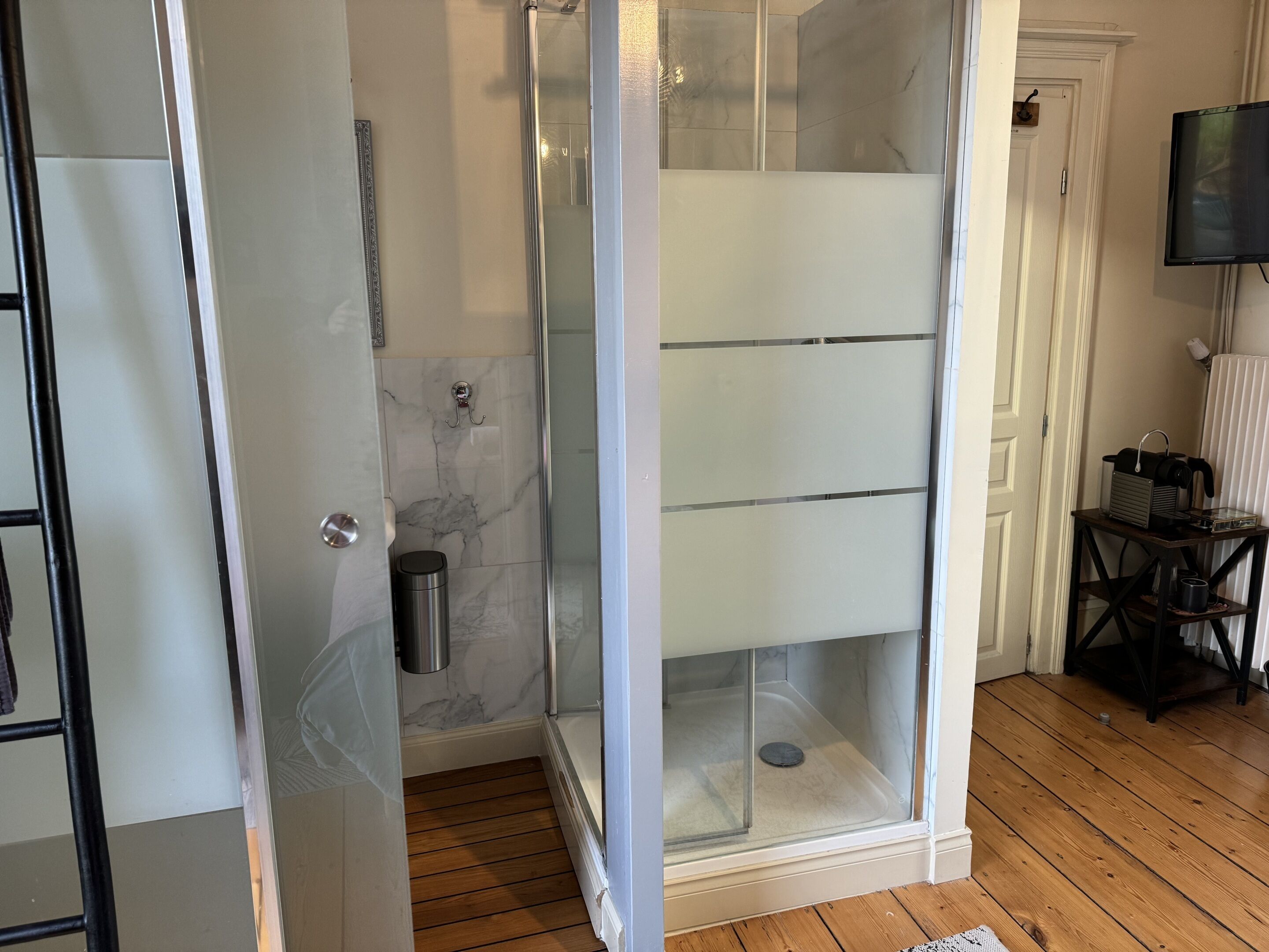 Un baño moderno con cabina de ducha de vidrio, suelo de madera y una mesita con lámpara.