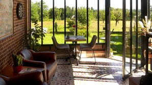 Una habitació amb paret de maó, un tirador, una taula amb cadires i vista a un jardí a través de grans finestres.
