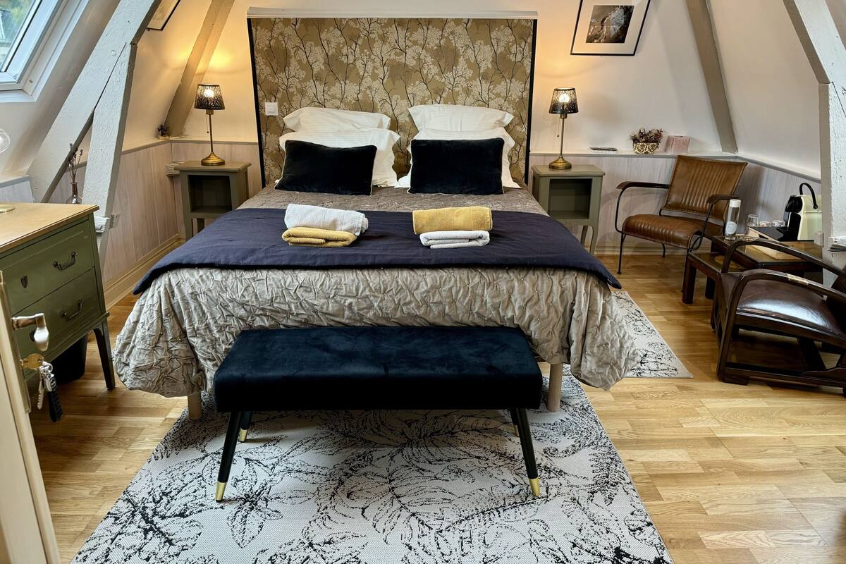 Een slaapkamer met een groot bed, twee nachtkastjes, een stoel, een bureau en een raam.