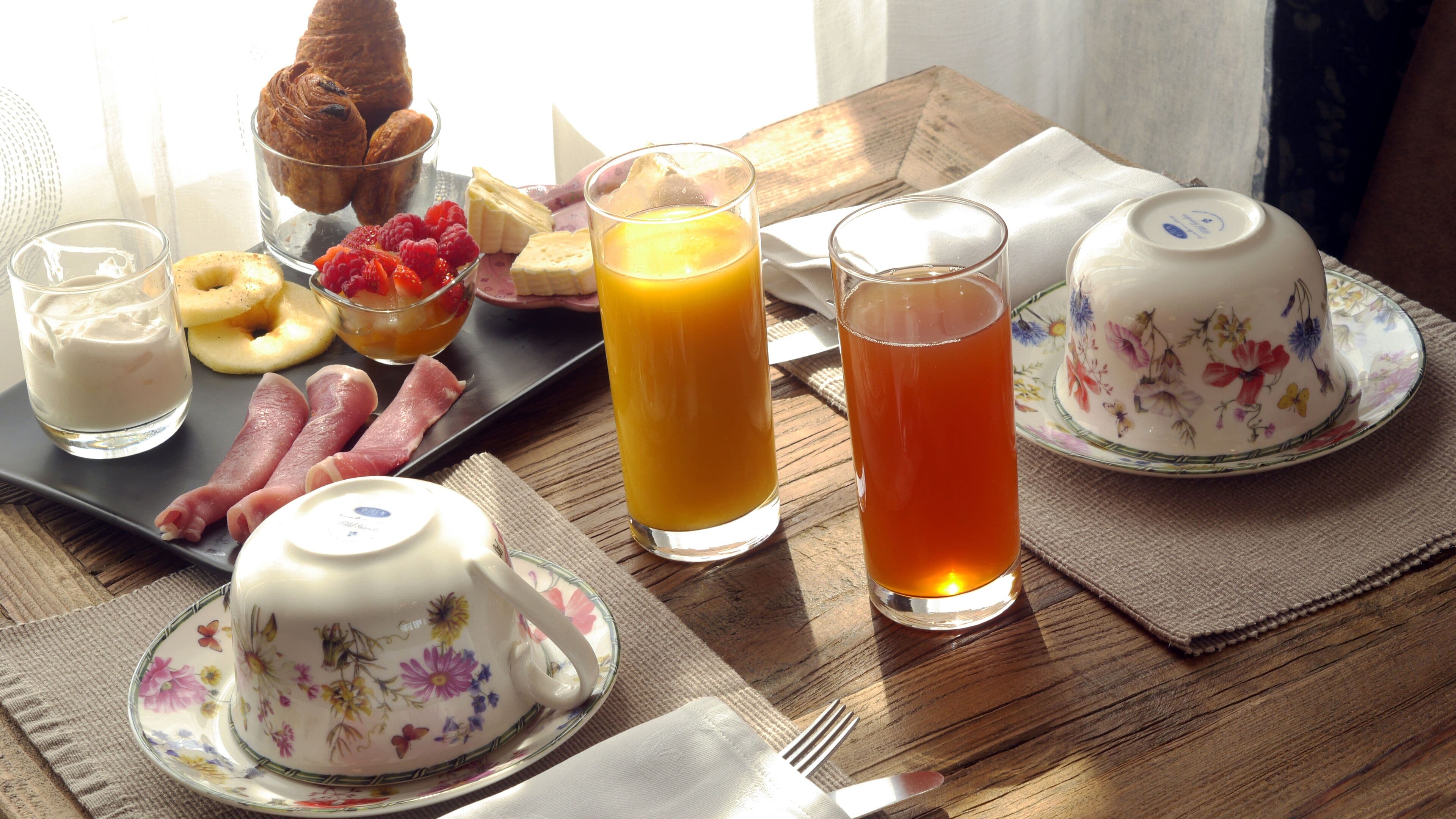 A breakfast table with croissants, fruit, cheese, and drinks.