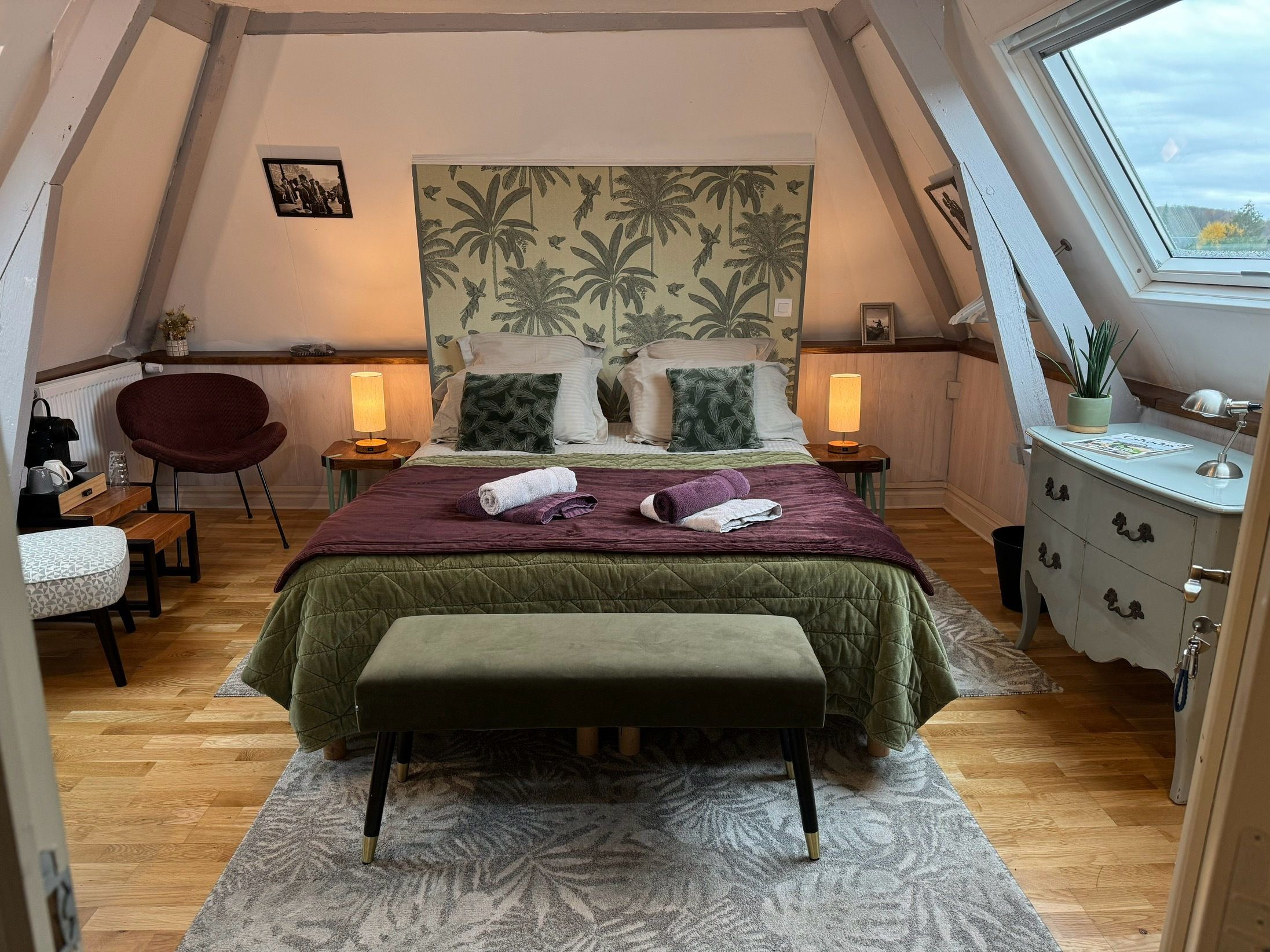 Ein gemütliches, dreieckiges Schlafzimmer mit Bett, Nachttischen, einem Sessel, einer Kommode und einem Fenster.