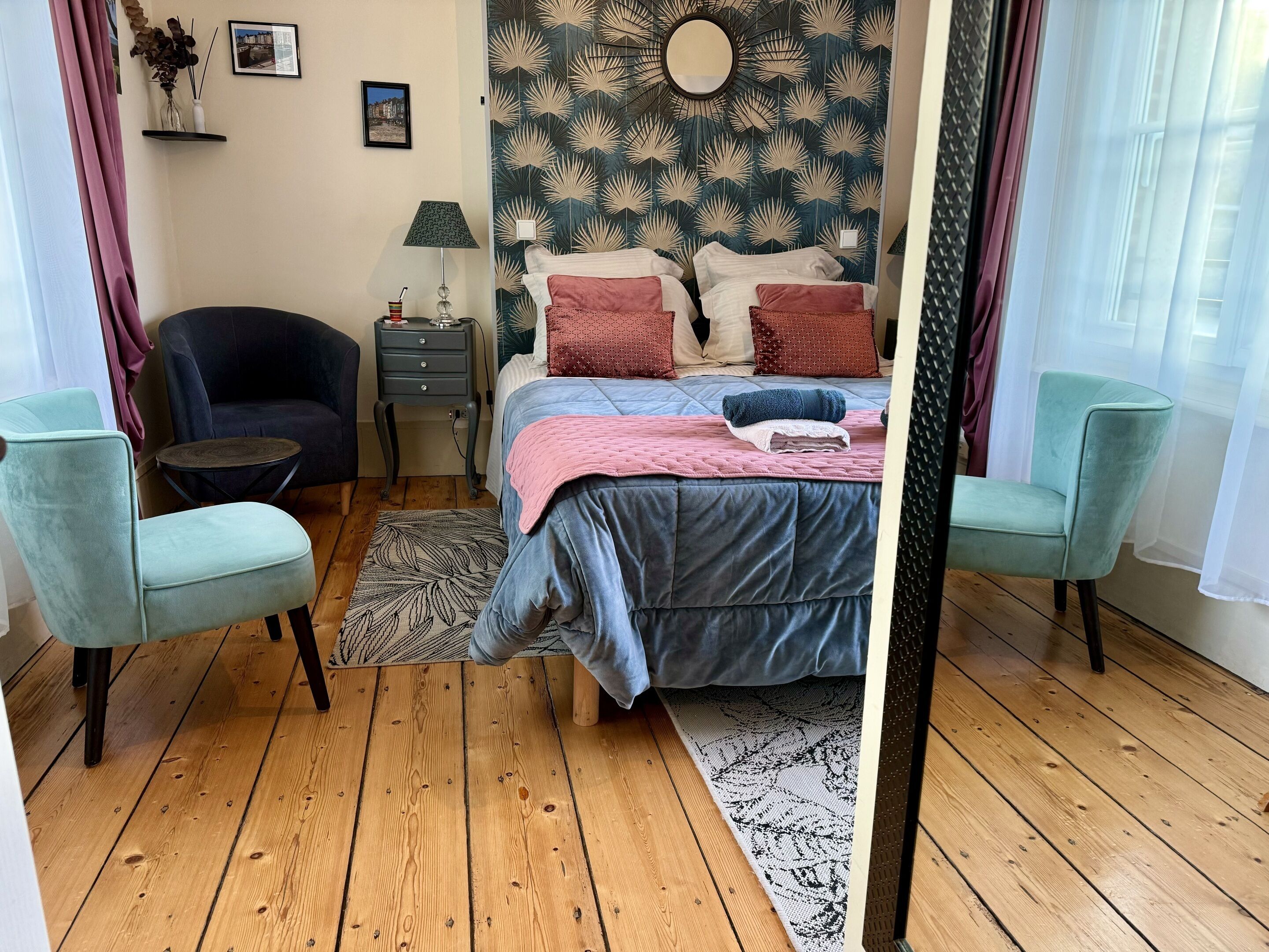A bedroom with a bed, two chairs, a nightstand, a lamp, and a patterned rug.