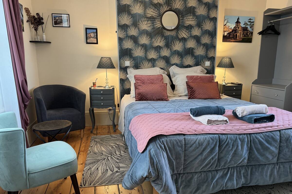 Een slaapkamer met een bed, twee nachtkastjes, een stoel, een kaptafel en een spiegel aan de muur.