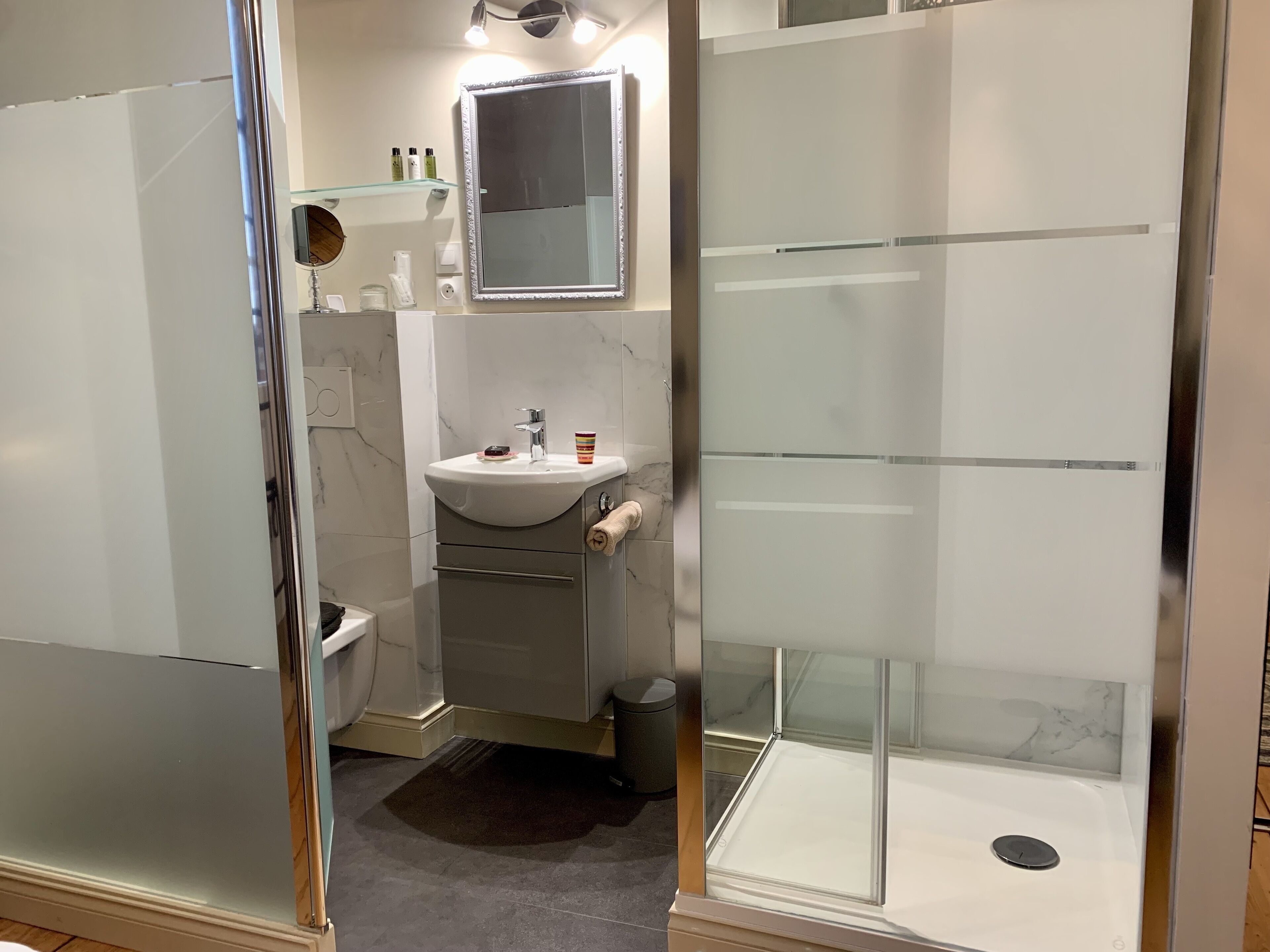 A modern bathroom with a glass shower enclosure, a sink with a marble countertop, and a mirror above the sink.